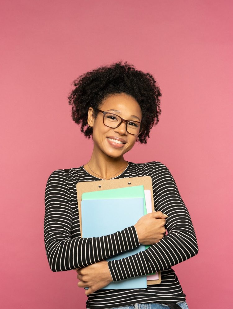 Happy Afro-American tutor or teacher woman isolated on pink studio wall. Education in high school